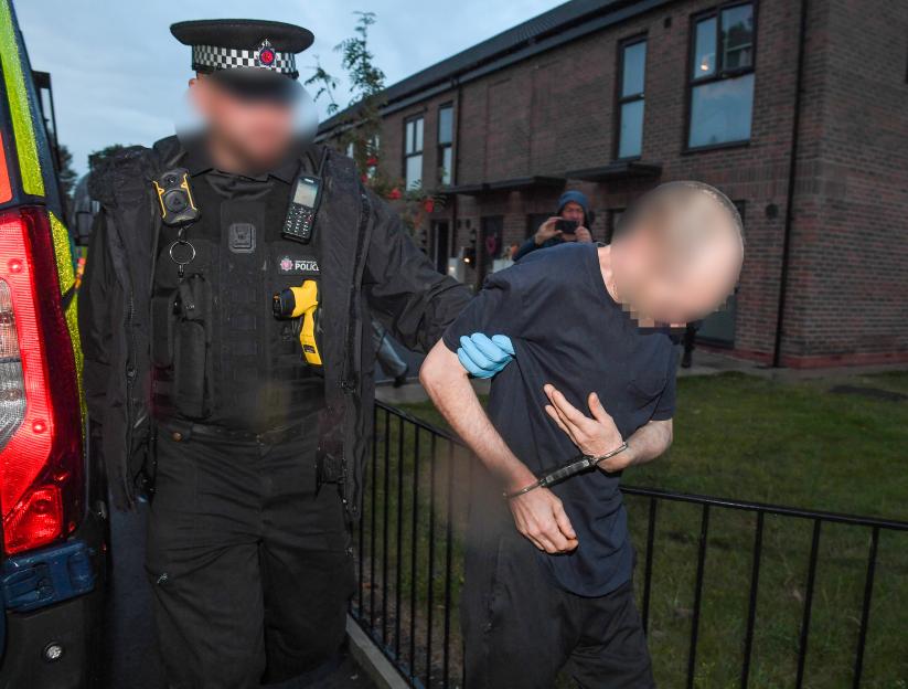 An arrested man in handcuffs being led to a police van by an officer.