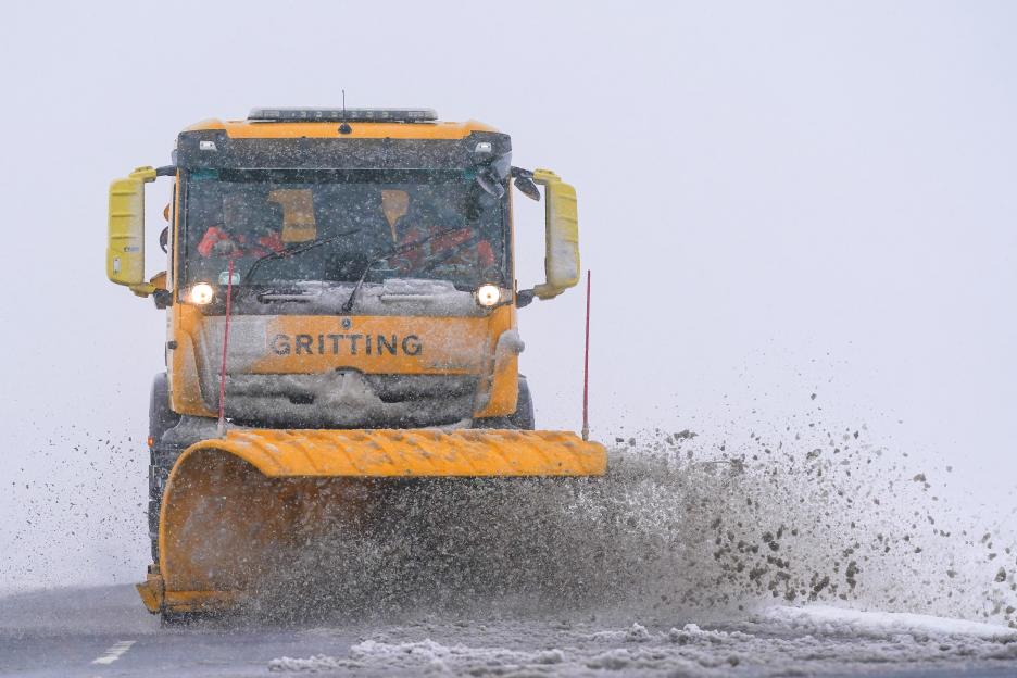 Yellow snow plough clearing snow from a road.