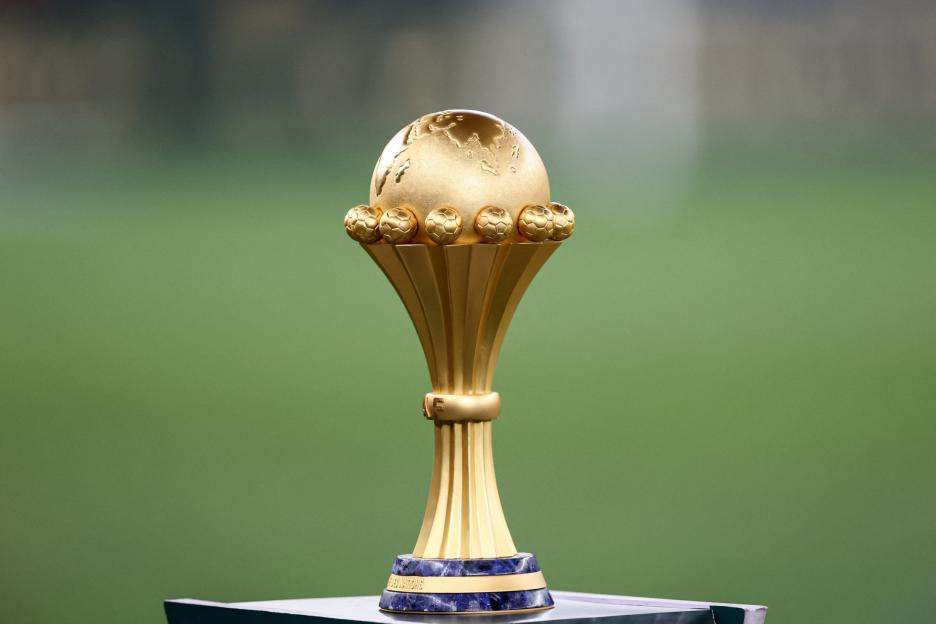 The golden Africa Cup of Nations trophy on a blue and gold base with a green background.
