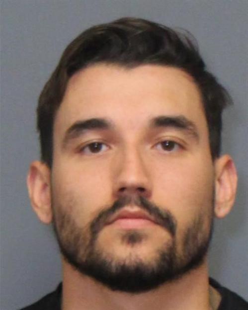 Mugshot of a man with dark hair and a beard, identified as a suspect charged with murder.