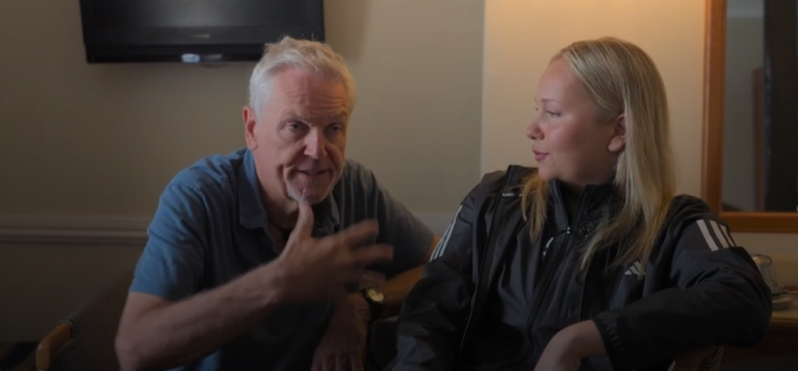 A man in a blue shirt gestures while talking to a woman in a black Adidas jacket.