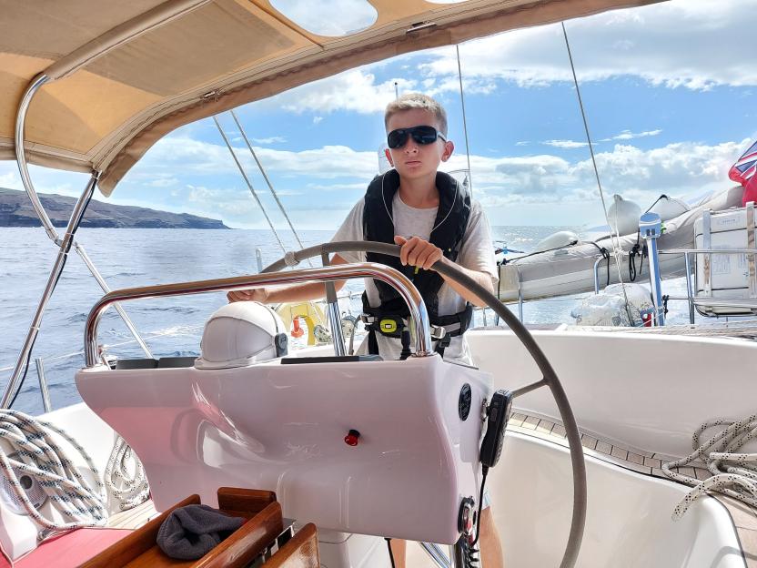 Eddie Jarman, wearing a life vest and sunglasses, steering a sailboat.