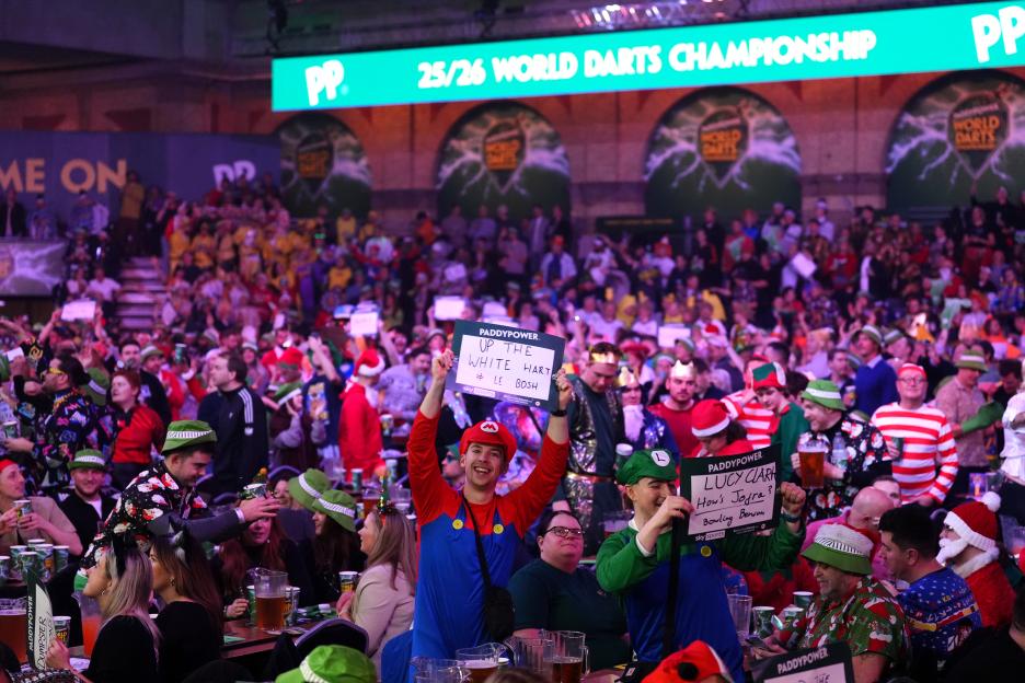 Fans dressed in various costumes, including Mario and Luigi, hold up signs at the Paddy Power World Darts Championship.