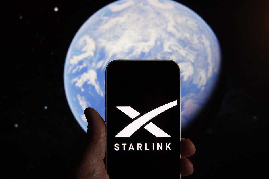 Illustration of a hand holding a mobile device displaying the Starlink logo, with an illustration of Earth in the background.