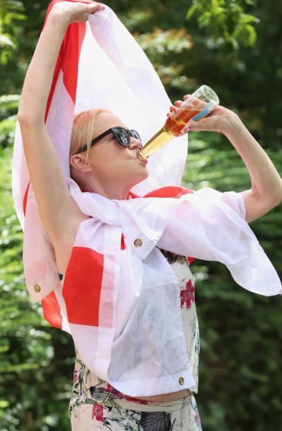 A woman wearing sunglasses and an English flag drinks from a bottle.