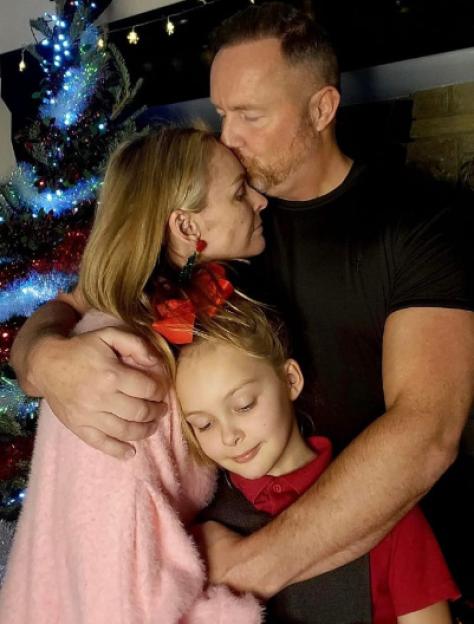 Mel Schilling with her husband and child in front of a Christmas tree.