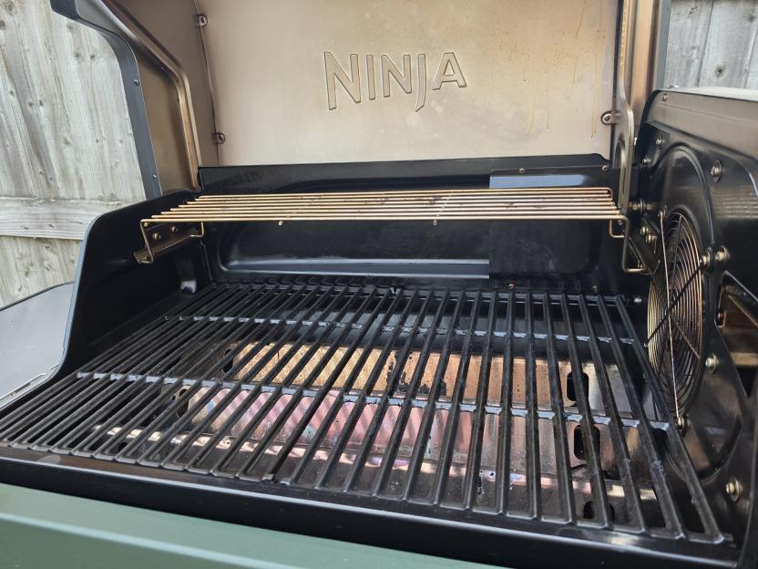 A Ninja outdoor grill with its lid open, revealing grill grates and a warming rack.
