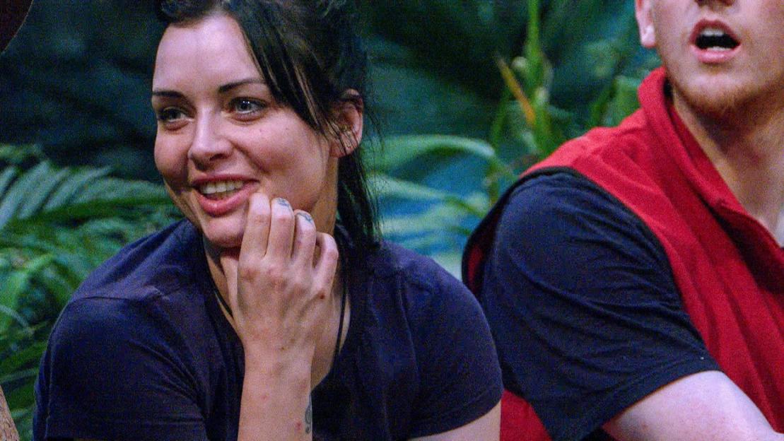Woman in a navy shirt smiling and resting her chin on her hand, next to a person in a red vest.