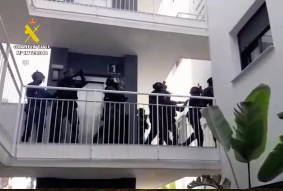 Spanish police officers conducting a raid on an apartment building balcony.