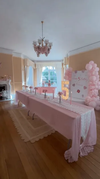 Stacey Solomon's dining room transformed with pink decorations for a 5th birthday party, featuring a long table with a pink cloth and candles, a lit-up number 5, and a pink balloon arch.