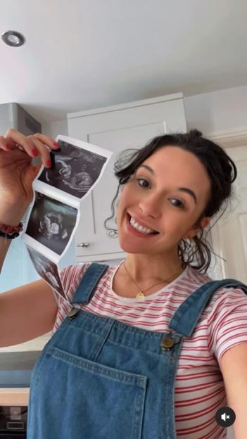 Charlotte Chilton smiling while holding up her 20-week baby scan images.