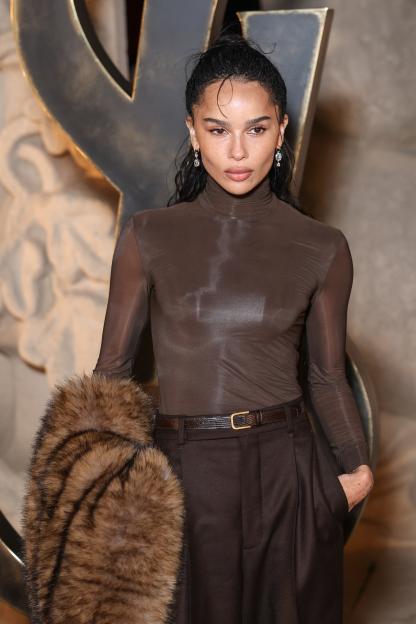 Zoe Kravitz in a brown turtleneck top, brown trousers with a belt, and a brown fur stole.