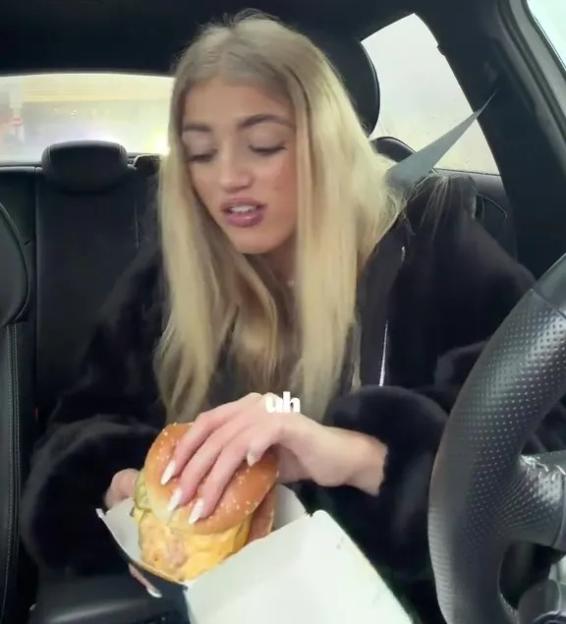 Princess Andre looking queasy while holding a burger in a car.