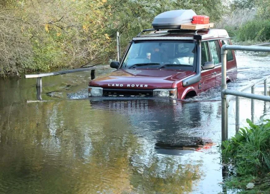 A red Land Rover Discovery drives through a deep flood, its front bumper submerged in water.