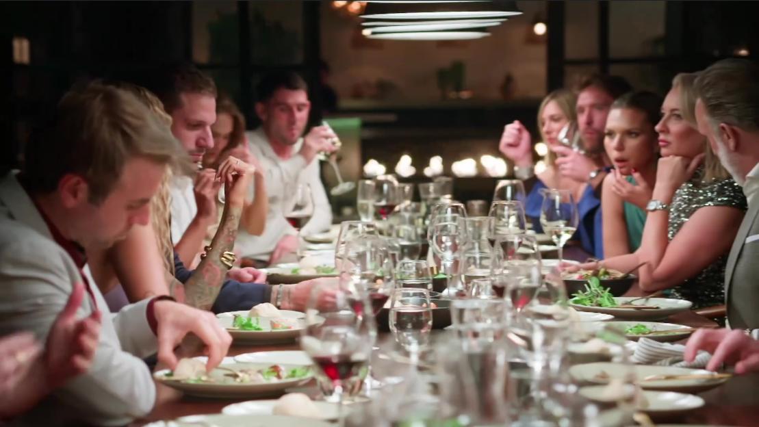 A group of people sitting at a long dinner table with plates and wine glasses.
