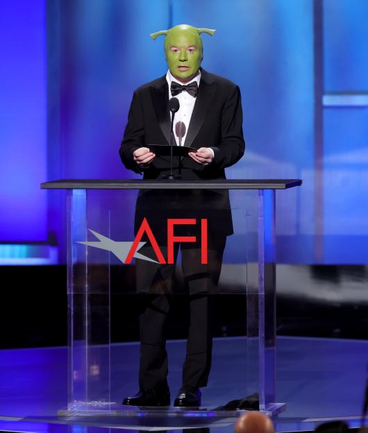 Mike Myers wearing a Shrek mask and a tuxedo, standing at a podium with the AFI logo.