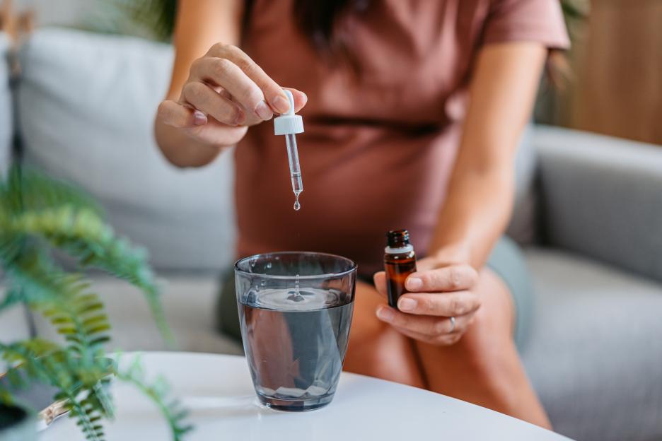 Mid-Adult Pregnant Asian Woman Putting Medicine Drops In A Glass Of Water