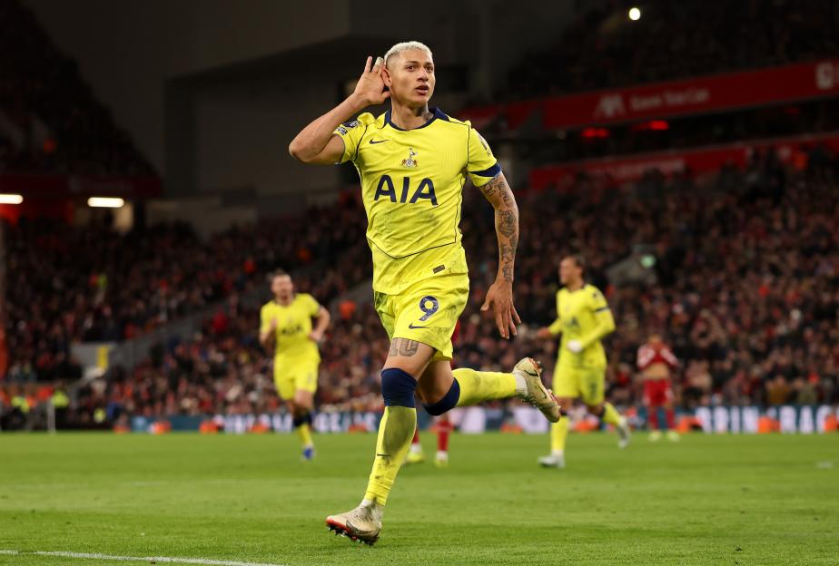 A male soccer player in a yellow jersey celebrating on the field, with the score Liverpool 1-1 Tottenham 89:15 visible on screen.