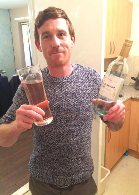 A man holds a glass of rosé wine and a nearly empty bottle of Pinot Grigio blush.