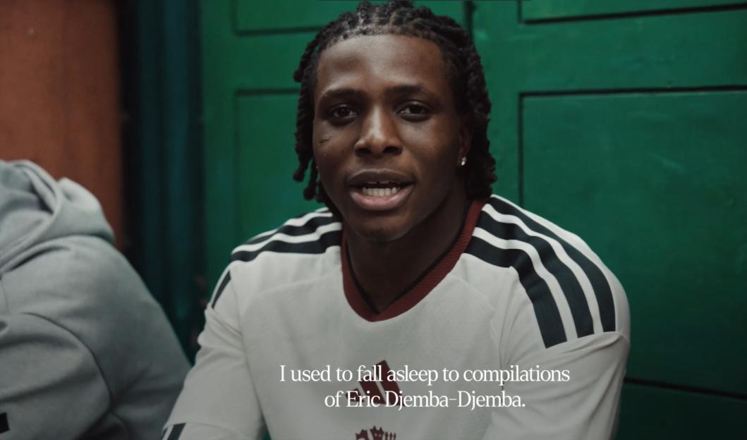 A man with braided hair and a white Adidas shirt is speaking, with the caption "I used to fall asleep to compilations of Eric Djemba-Djemba."