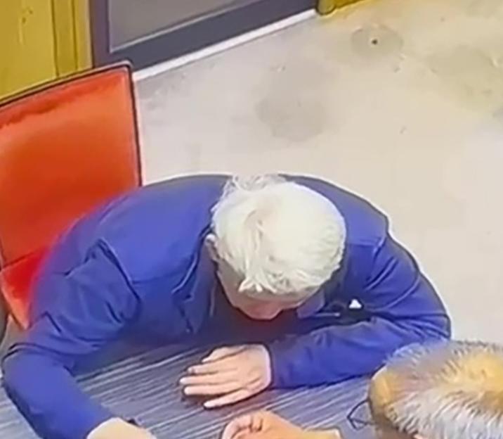 CCTV footage of a man in a blue jacket attempting to swallow a ring at a jeweler's table.