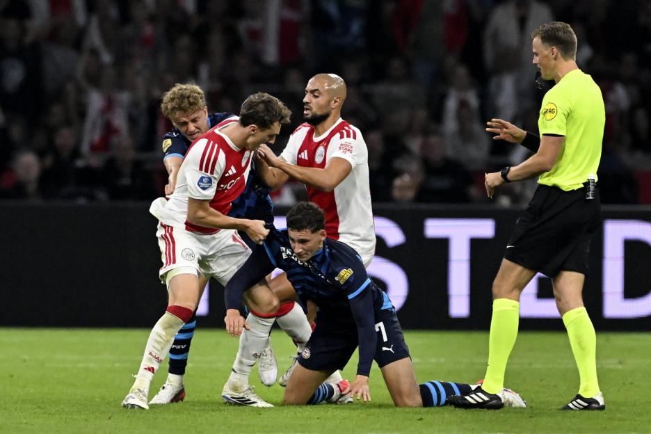 Ajax and PSV players in a scuffle on the field as the referee watches.