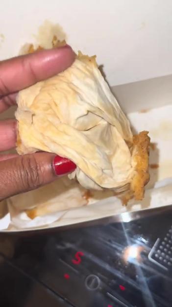 Hand holding a fried chicken wing covered in a paper napkin.