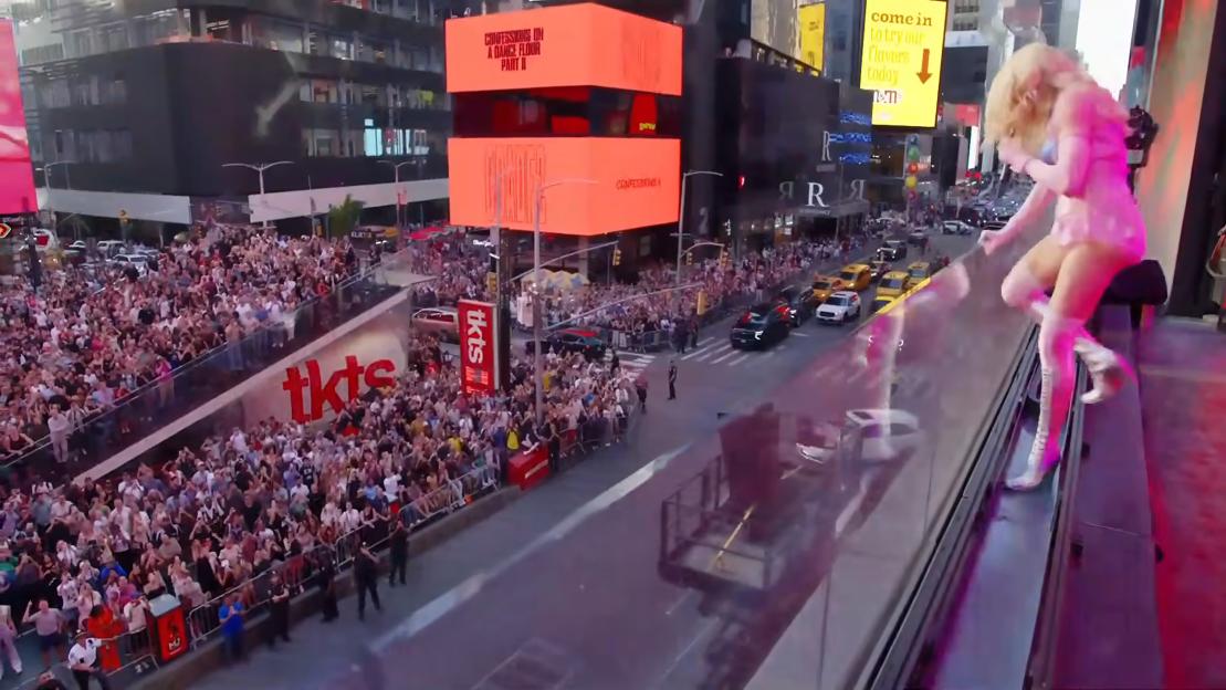 Madonna leaning over a barrier with a crowd of fans below in Times Square.