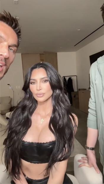 Kim Kardashian with dark, wavy hair, wearing a black leather top, with a man on either side.