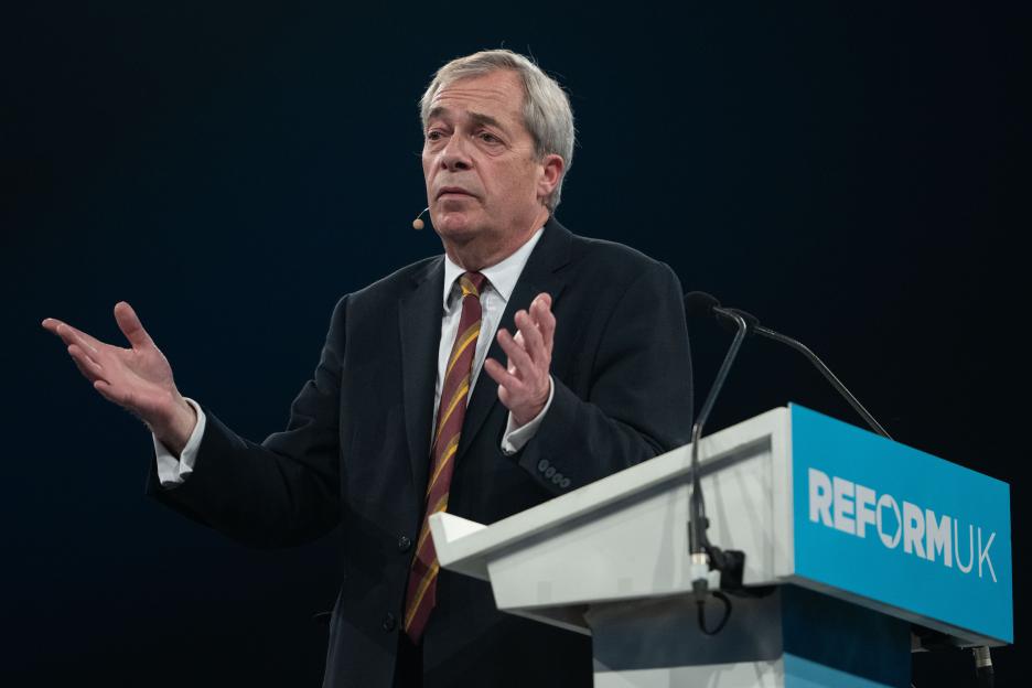 Nigel Farage, leader of Reform UK, speaking at a rally with arms outstretched and a microphone on his cheek.