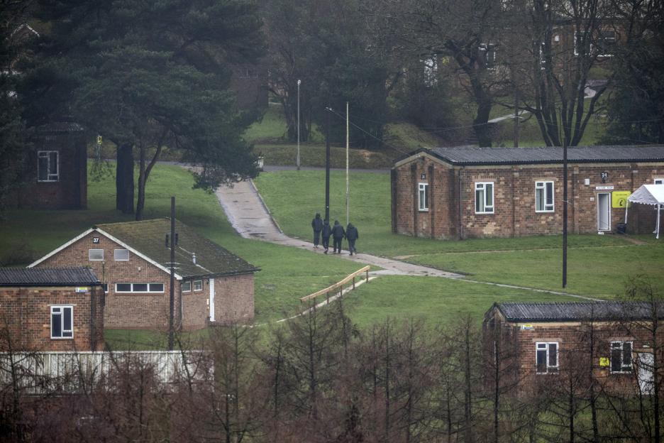 Four migrants walk along a path between barracks at the former military site of Crowborough Training Camp.