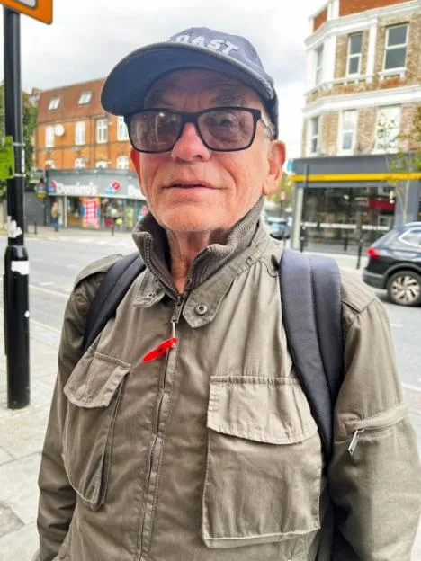 A man wearing glasses, a cap, and a jacket on Uxbridge Road in London.