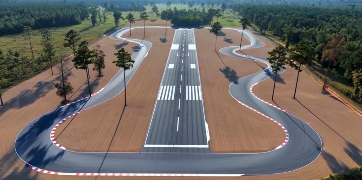 Aerial view of a runway flanked by winding race tracks and pine trees.