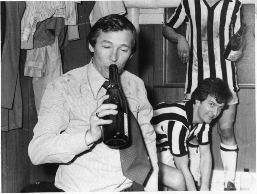 St. Mirren manager Alex Ferguson drinking champagne from a bottle in a locker room.