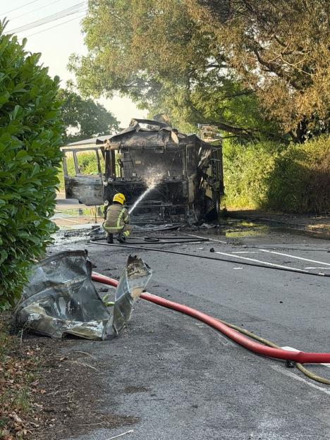 A burned-out fire engine on the side of a road, emitting smoke and ash.