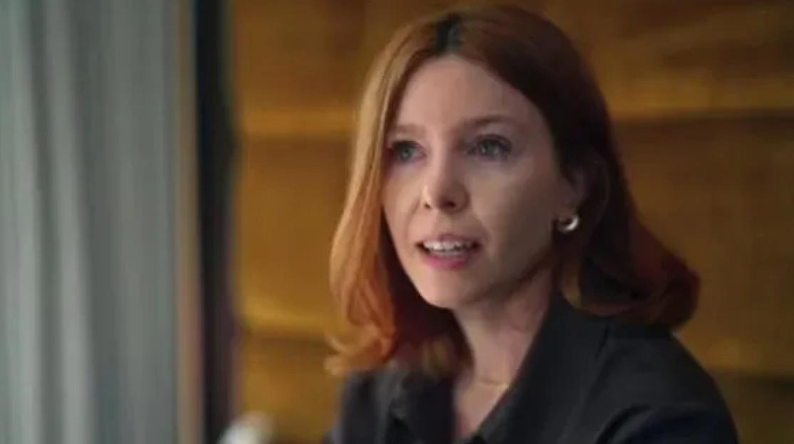 Stacey Dooley with red hair, wearing a black top, appears to be holding back tears as she speaks.