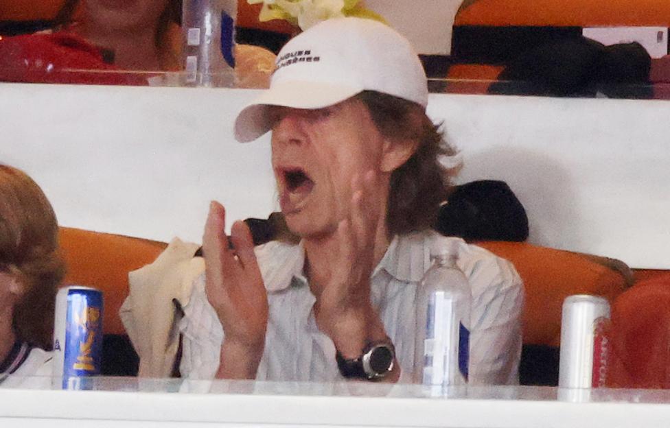 Mick Jagger claps while wearing a white baseball cap, watching the Norway vs England World Cup match.