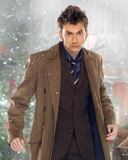 David Tennant as the Tenth Doctor in a brown pinstripe suit, blue shirt, striped tie, and a long brown coat, in a snowy landscape.
