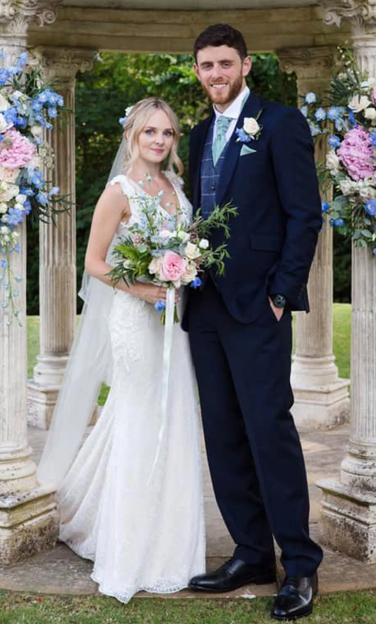 Wedding photo of Pc Andrew Harper and his wife Lissie, standing under a gazebo decorated with pink and blue flowers.