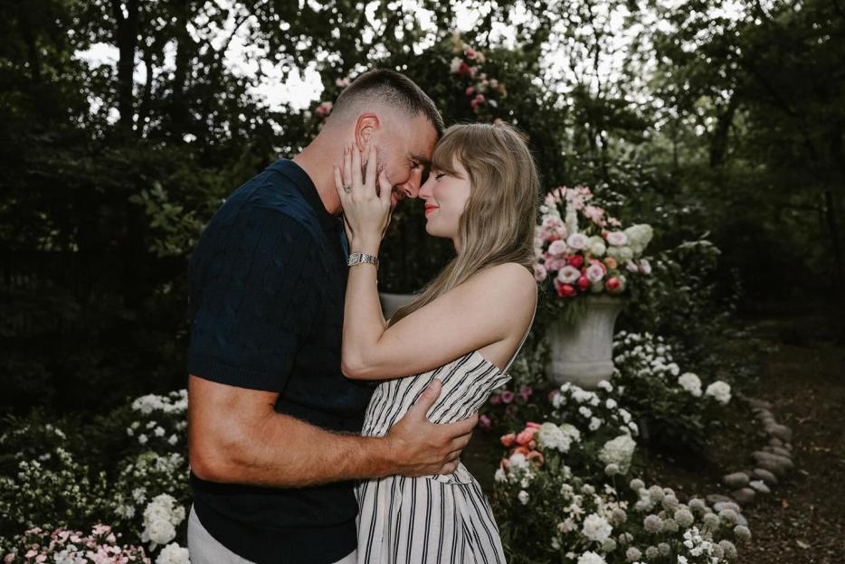 Taylor Swift and Travis Kelce embracing with their foreheads touching, surrounded by flowers.