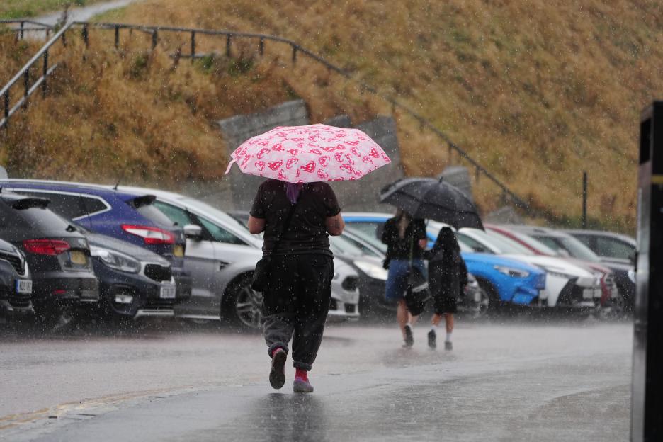 Two people shelter from the rain under a black umbrella.