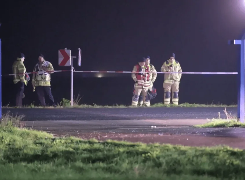 First responders stand behind a police tape barrier at Leipzig Airport at night.