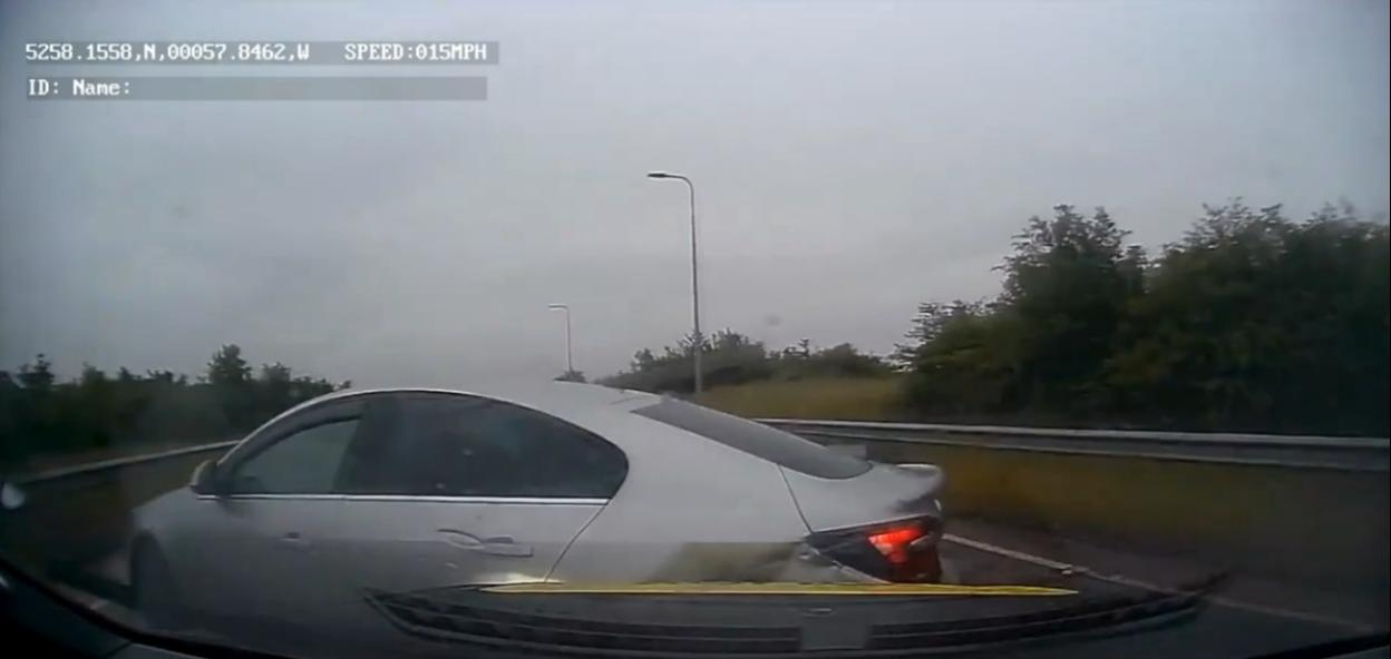 A silver sedan on a highway with visible damage to its rear bumper and taillight, viewed from inside another car.