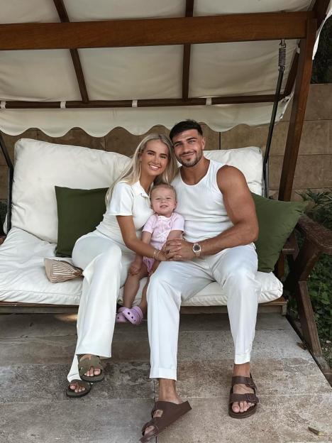 Molly Mae Hague, Tommy Fury, and their baby daughter Bambi sitting on a porch swing.