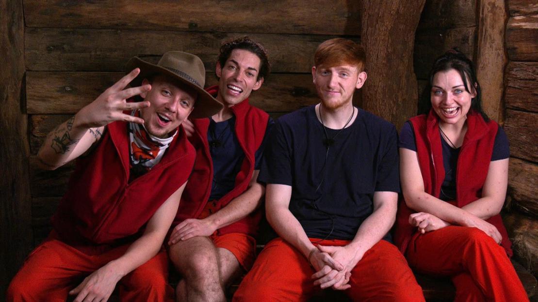 Four contestants from "I'm a Celebrity... Get Me Out of Here!" smiling and sitting in a wooden hut.