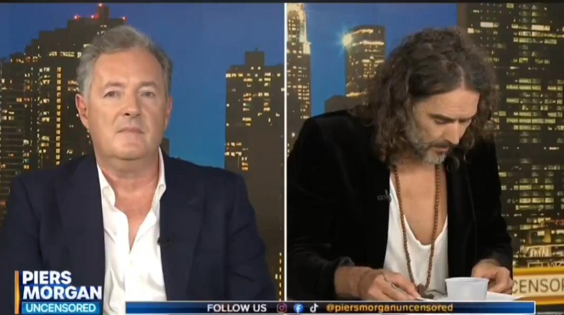 Piers Morgan on the left and Russell Brand on the right with a city skyline in the background.