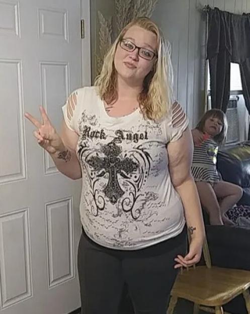 A woman in a "Rock Angel" t-shirt making a peace sign, with a child on a couch in the background.