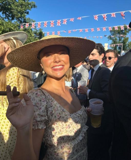 A woman in a straw hat holding a cigar and a drink, with Union Jack bunting in the background.