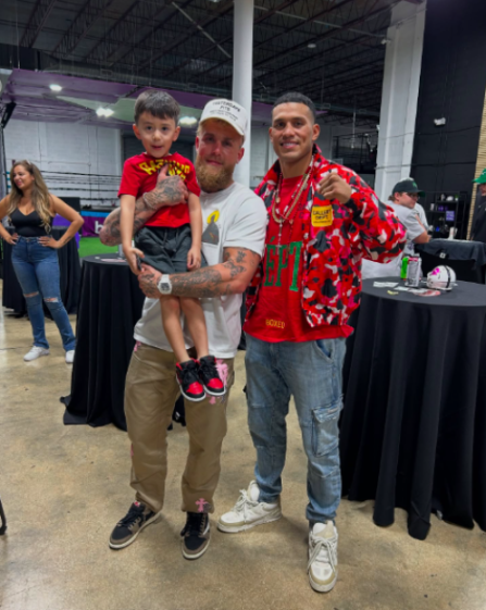 Jake Paul holding a young boy while standing next to a boxer.