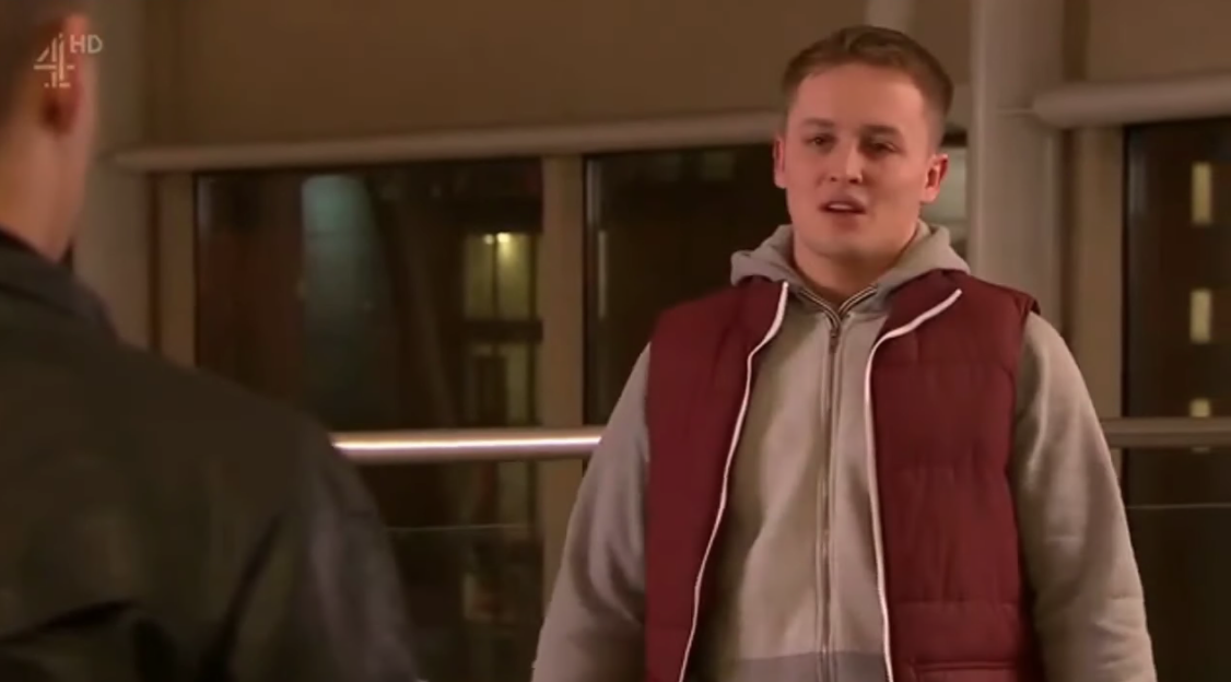Alfie Brown-Skyes from Hollyoaks wearing a maroon puffer vest over a grey hoodie.